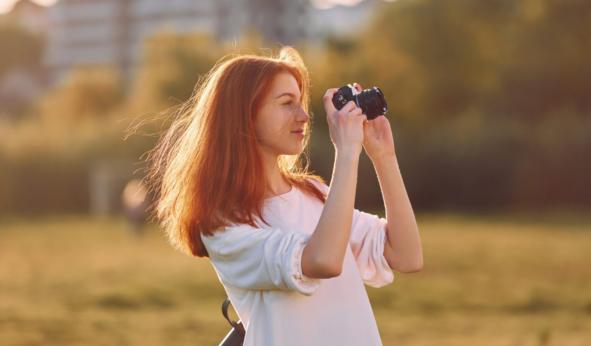 Photographer is with camera. Young girl is on the field at sunny daytime having nice weekend.